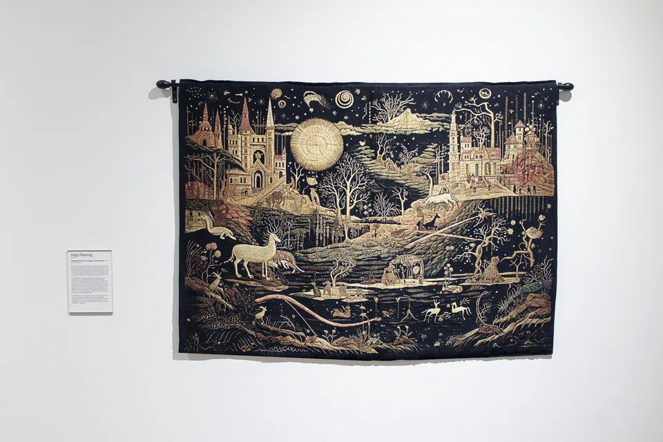 A dark tapestry depicts two castles, a large golden orb, branching trees and pale animals crossing an intricate landscape.