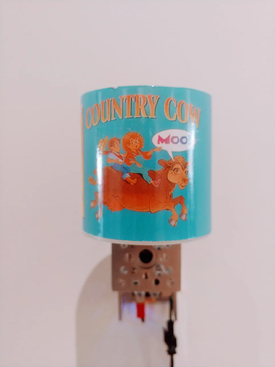 A turquoise Country Cow novelty can with a cartoon cow is mounted above an exposed motorized mechanism.