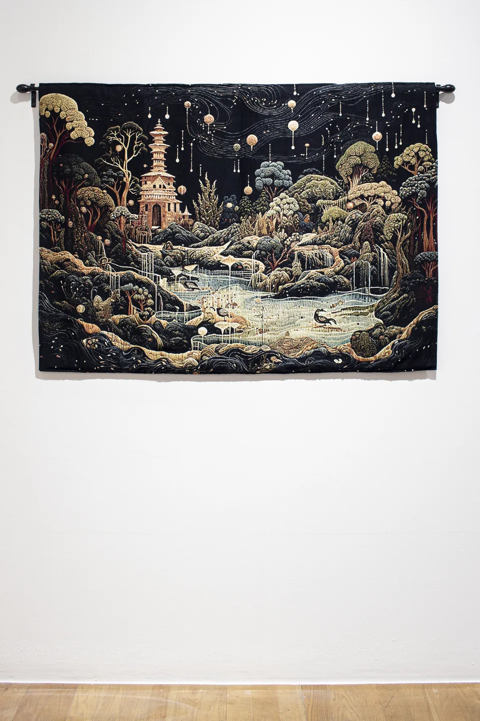 The tapestry hangs on a black rod, displaying a pagoda, waterfalls, winding streams and small creatures beneath a dark sky.