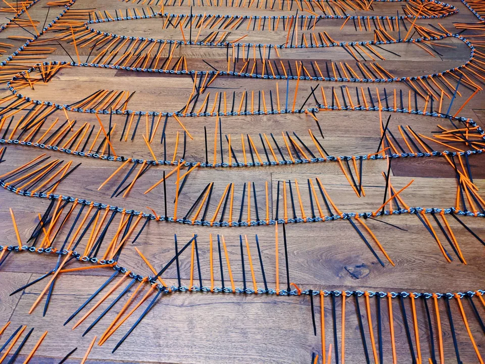 Close view of orange and black cable ties attached to the links of a chain on a wooden floor.